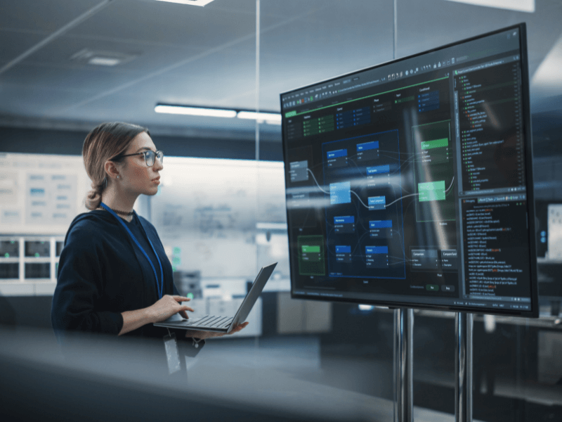 Person examining a software diagram on a large digital screen in a modern office.