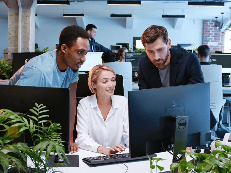 Three colleagues working together in an office, focused on a computer screen