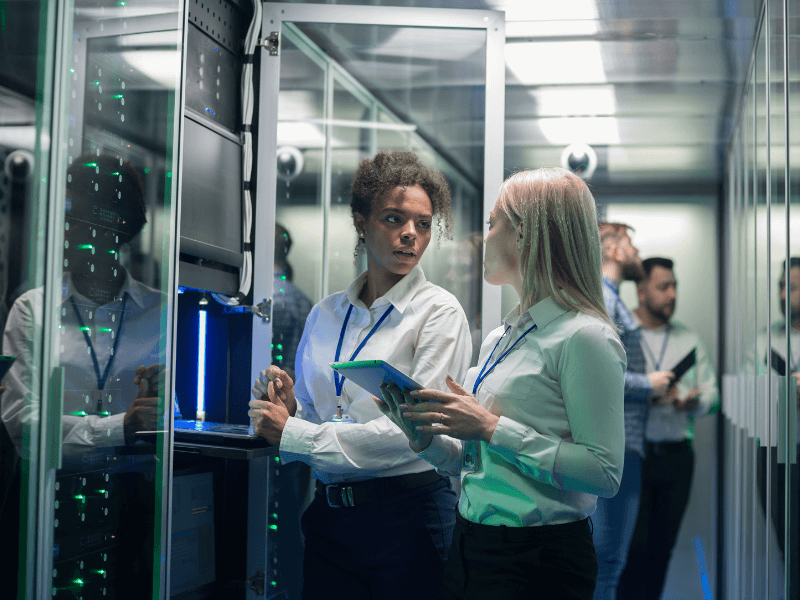 Two professionals in a server room with a tablet and server equipment