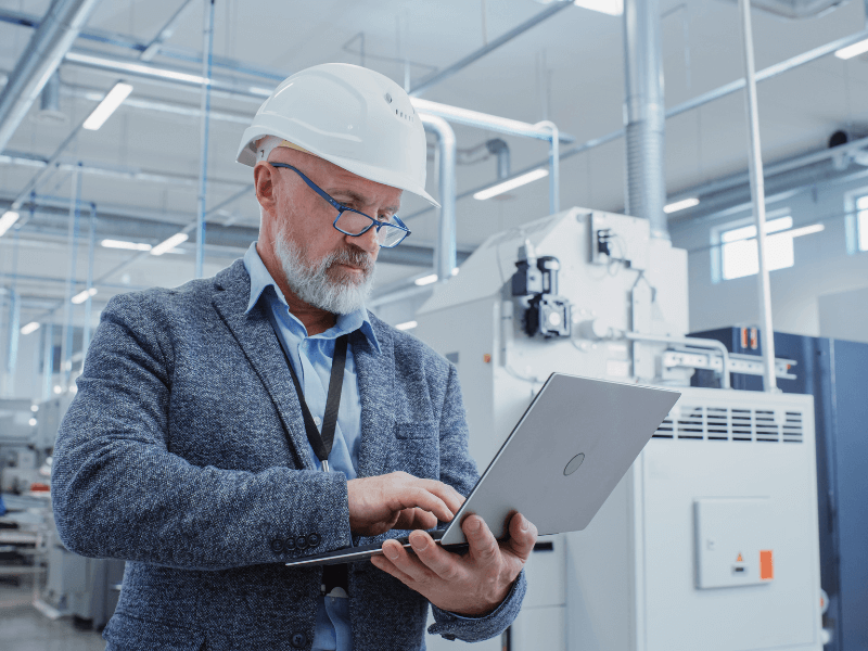 Man in a hard hat using a laptop in an industrial environment.