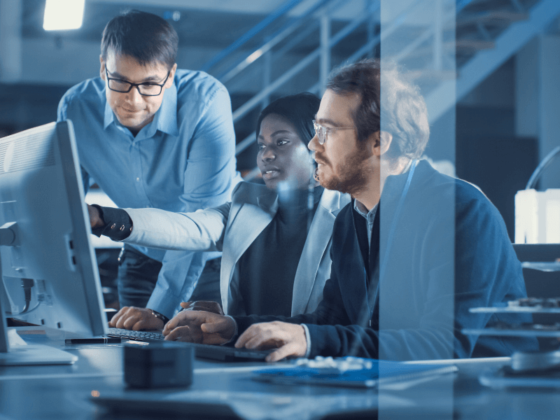 Three people in an office, collaborating at a computer workstation.