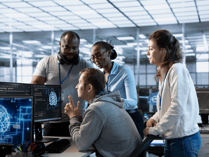 A group of four people in an office setting focused on computer monitors displaying digital brain images.