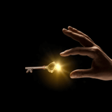 A hand reaching towards a glowing key on a black background.