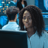 A woman with curly hair working at a computer in a modern office setting.