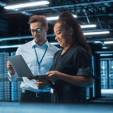 Two people in a server room looking at a laptop.