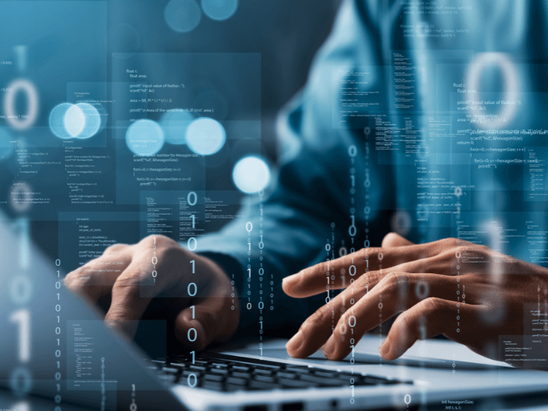 Hands typing on a laptop with overlaid code and binary numbers.
