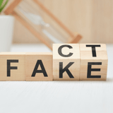 Wooden blocks spelling “FAKE” with the first block rotated to show “C,” suggesting 
