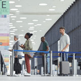 Four people standing in line at an airport, each holding different items.