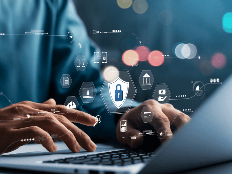 Hands typing on a laptop with floating icons of digital security above